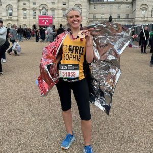 A woman standing at the finishing line of the London Marathon holding her medal