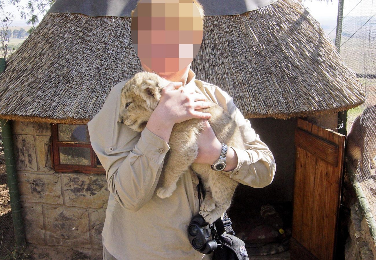 A person cradling a tiny lion cub