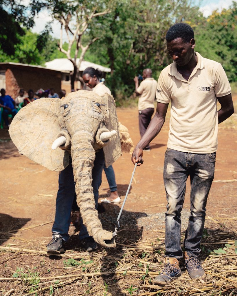 A man walks alongside someone dressed in an elephant puppet head