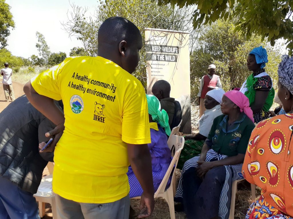 A man facing away from the camera is wearing a yellow T-shirt with the slogan 'A healthy community, a healthy environment' with a group of people sat in front of him