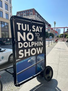 A framed poster on wheels says 'TUI, say no to the dolphin show'