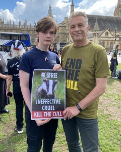 Hector Bateman stands next to Chris Packham, holding a poster with a photo of a badger and the words 'Ineffective. Cruel. Kill The Cull'