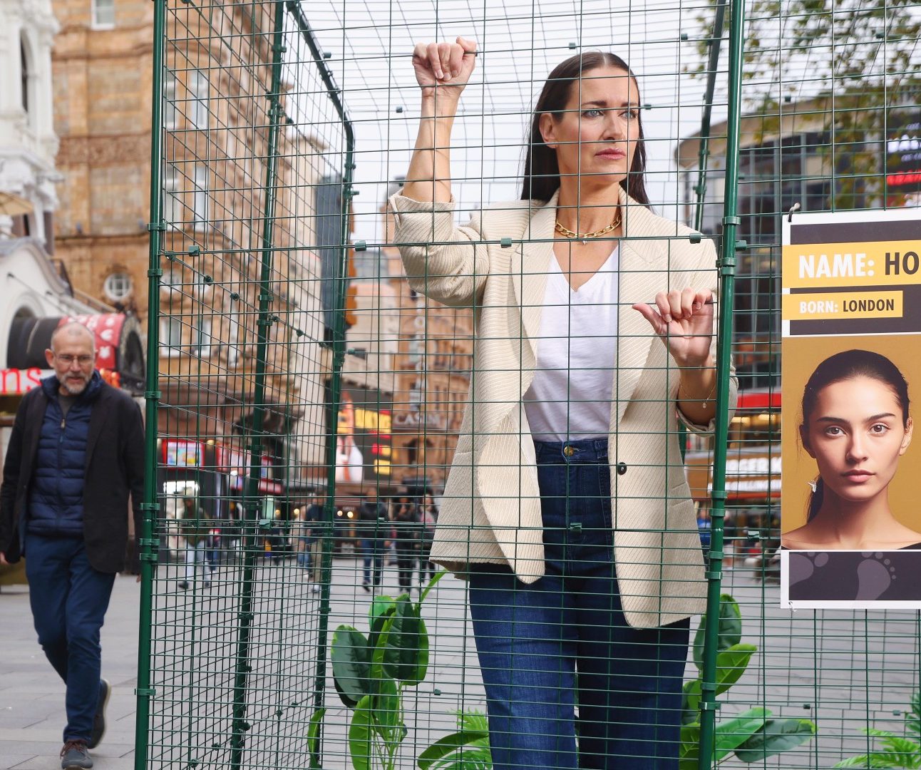 A photo of a woman in a small cage in central London, as people walk past looking at her