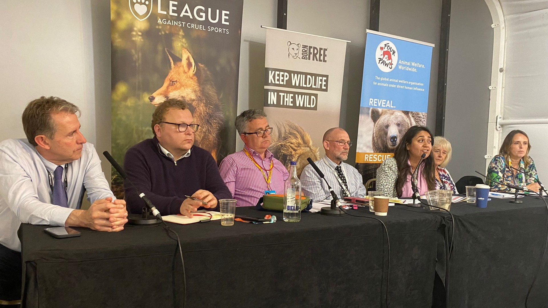 A group of people sitting at a long table at a conference, with charity banners in the background