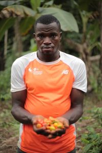 A pepper Farmer in Dja, Cameroon, wearing an orange t-shirt and holding peppers in both hands in front of him