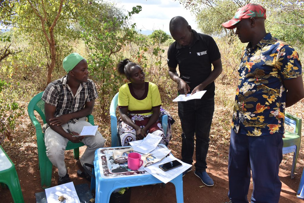 A member of Born Free staff in a black T-shirt is showing a booklet to local community members, with more documents on a table in front of them