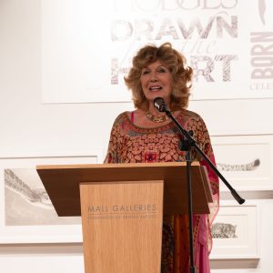 Rula Lenska hosting Drawn From the Heart behind a lectern