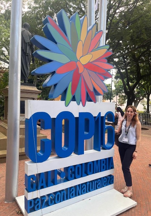 A woman standing next to a colourful sign for COP16