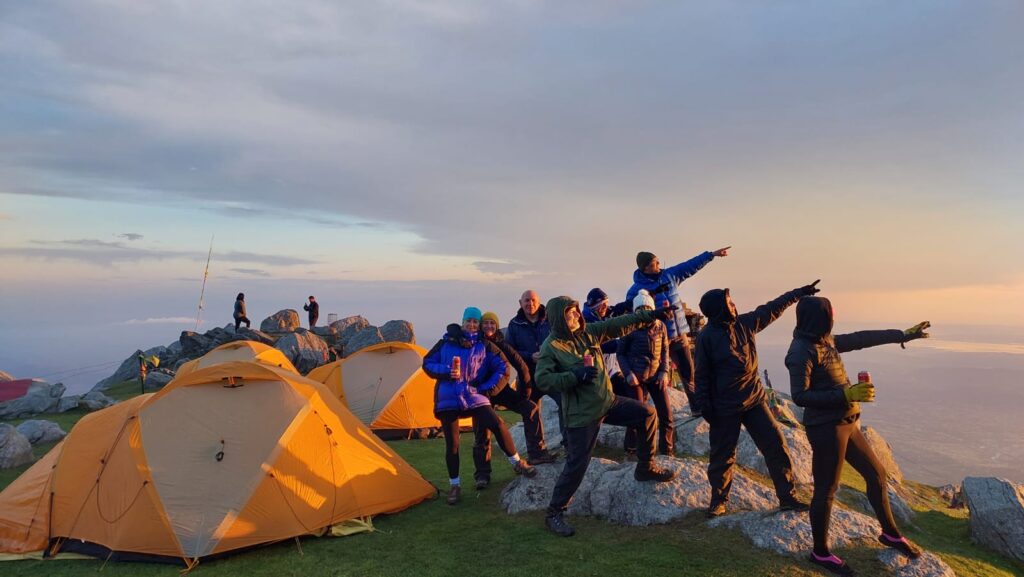 A group of people standing at the top of a mountain pointing into the distance