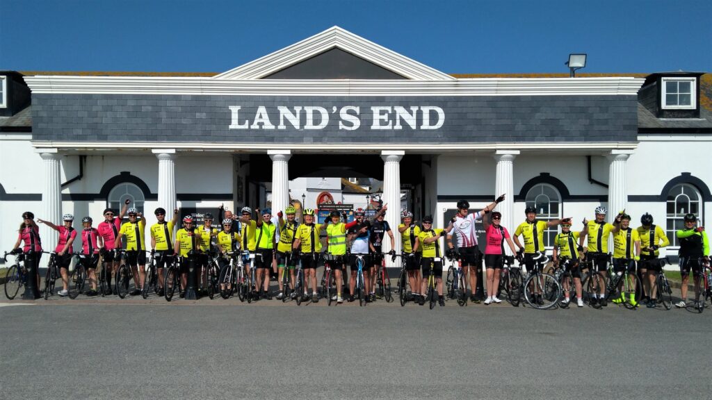 A large group of cyclists with their bikes standing outside a building with a Large Lands End sign